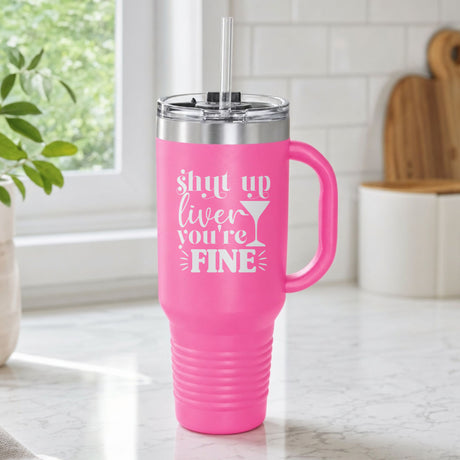 Pink 40 oz tumbler with handle and straw laser engraved with "Shut Up Liver, You're Fine", on a kitchen counter