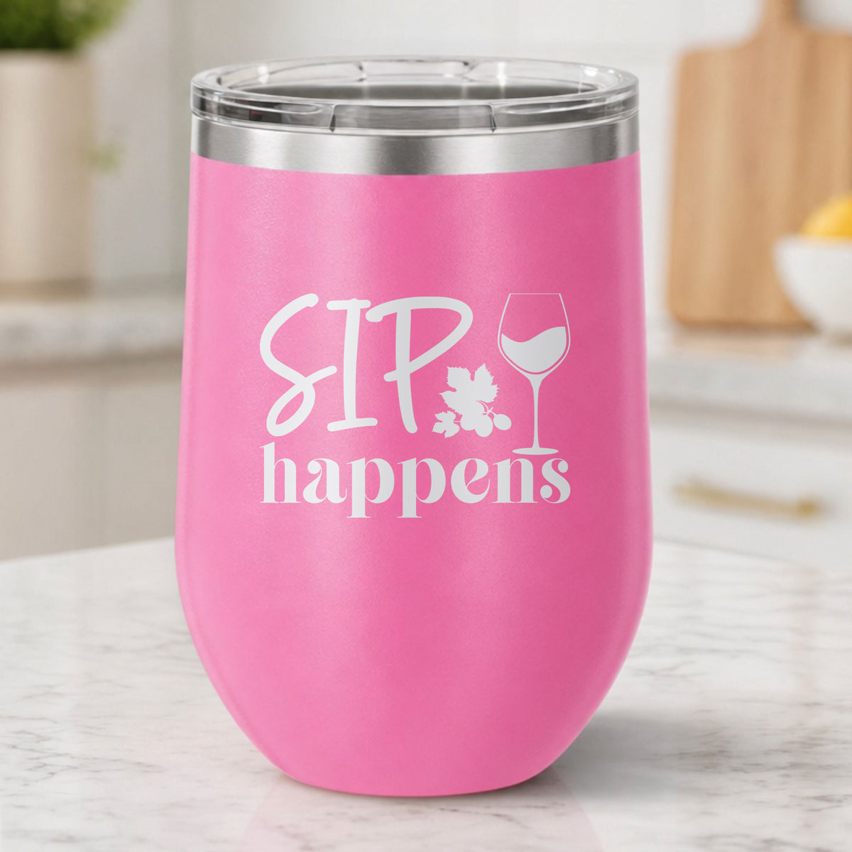 Pink 12 oz stemless wine tumbler laser engraved with "Sip Happens", on a kitchen counter