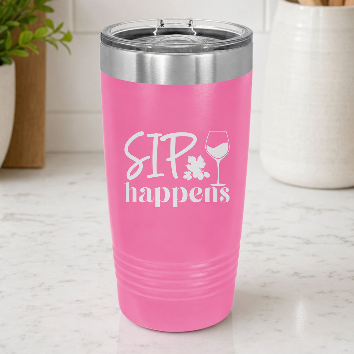 Pink 20 oz tumbler laser engraved with "Sip Happens", on a kitchen counter