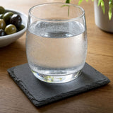 Square slate coaster on a wood table holding a glass of sparkling water
