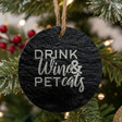 Round black slate Christmas ornament hanging on a Christmas tree, laser engraved in white with "Drink Wine and Pet Cats"