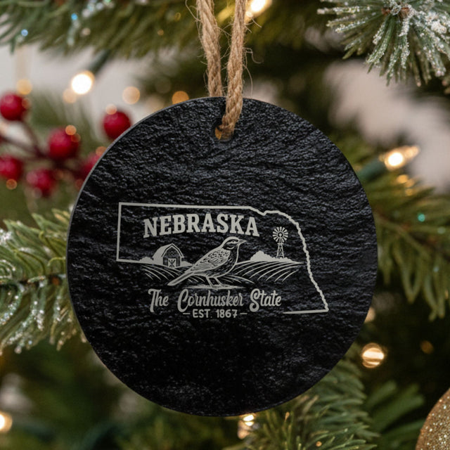 Round slate Christmas ornament laser engraved with a Nebraska design of a western meadowlark, a barn and a windmill