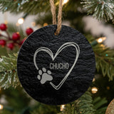 Round slate Christmas ornament engraved with a sketched heart, a paw print and the name Chucho, hanging on a tree