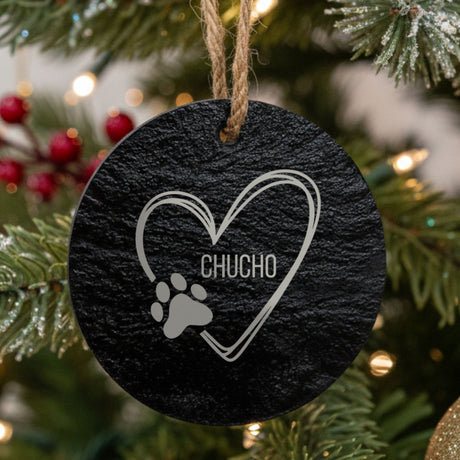 Round slate Christmas ornament engraved with a sketched heart, a paw print and the name Chucho, hanging on a tree