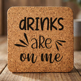 Square cork coaster laser engraved with "Drinks Are On Me", hand lettered design