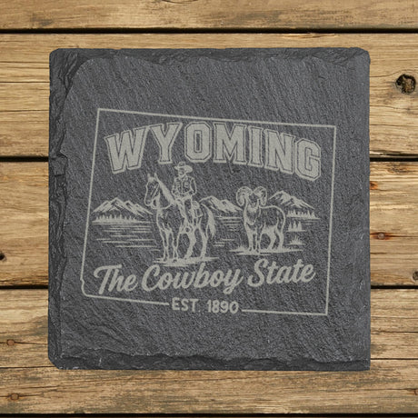 Wyoming square slate coaster engraved with the state outline, a cowboy on horseback, a bighorn sheep and mountains, "The Cowboy State"