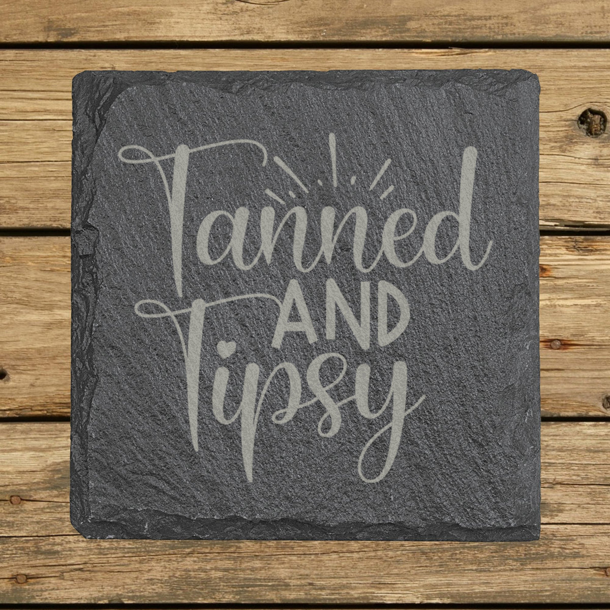 Square slate coaster laser engraved with "Tanned and Tipsy"