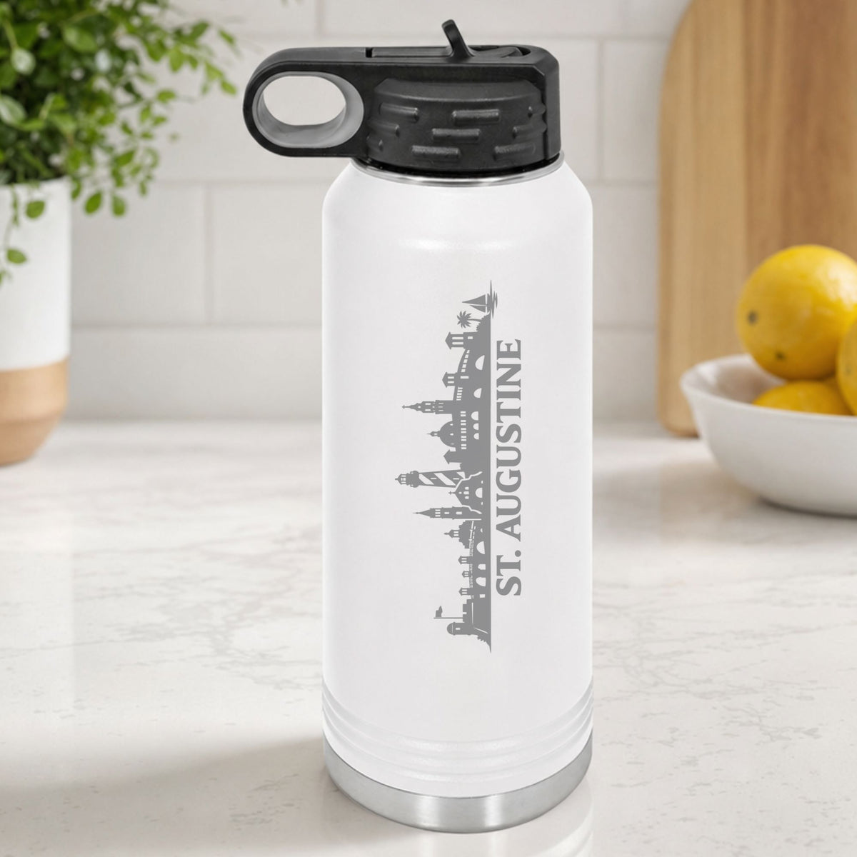 White 32 oz insulated water bottle laser engraved with the St. Augustine, Florida skyline running up the side, standing on a kitchen counter