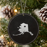Black leatherette round Christmas ornament laser engraved with the Alaska Heart Accent design, hanging on a tree