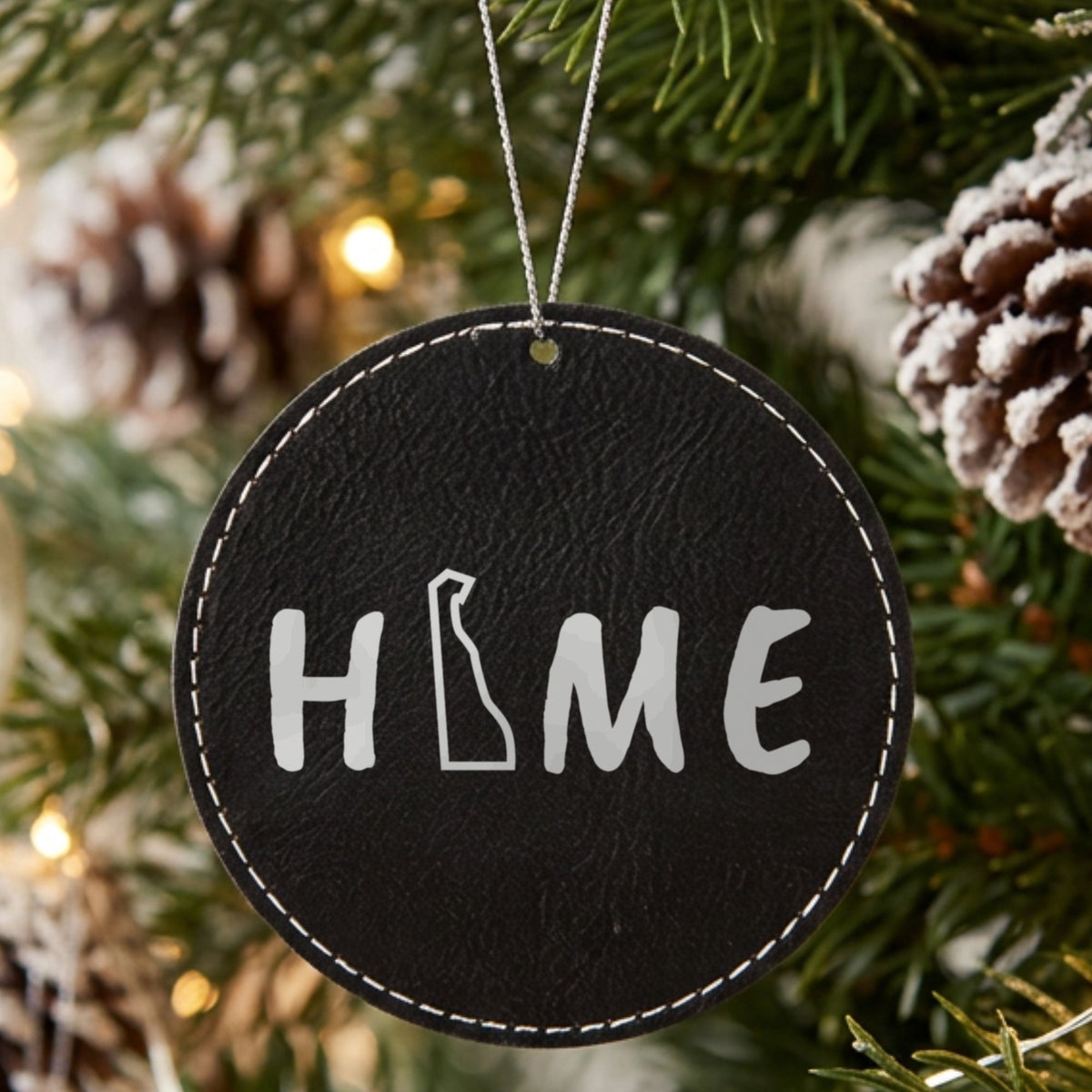 Black leatherette round Christmas ornament laser engraved with the Delaware HOME Outline design, hanging on a tree