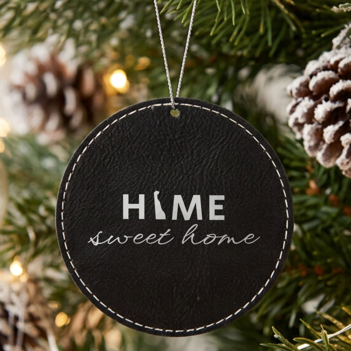 Black leatherette round Christmas ornament laser engraved with the Delaware Home Sweet Home design, hanging on a tree