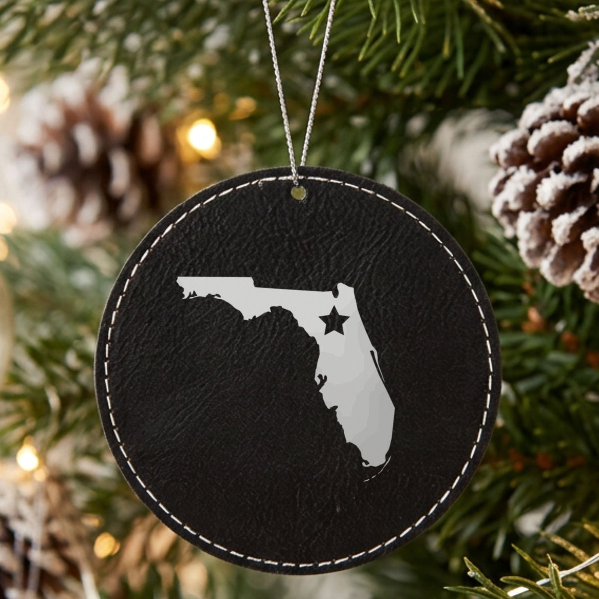 Black leatherette round Christmas ornament laser engraved with the Florida Star Accent design, hanging on a tree