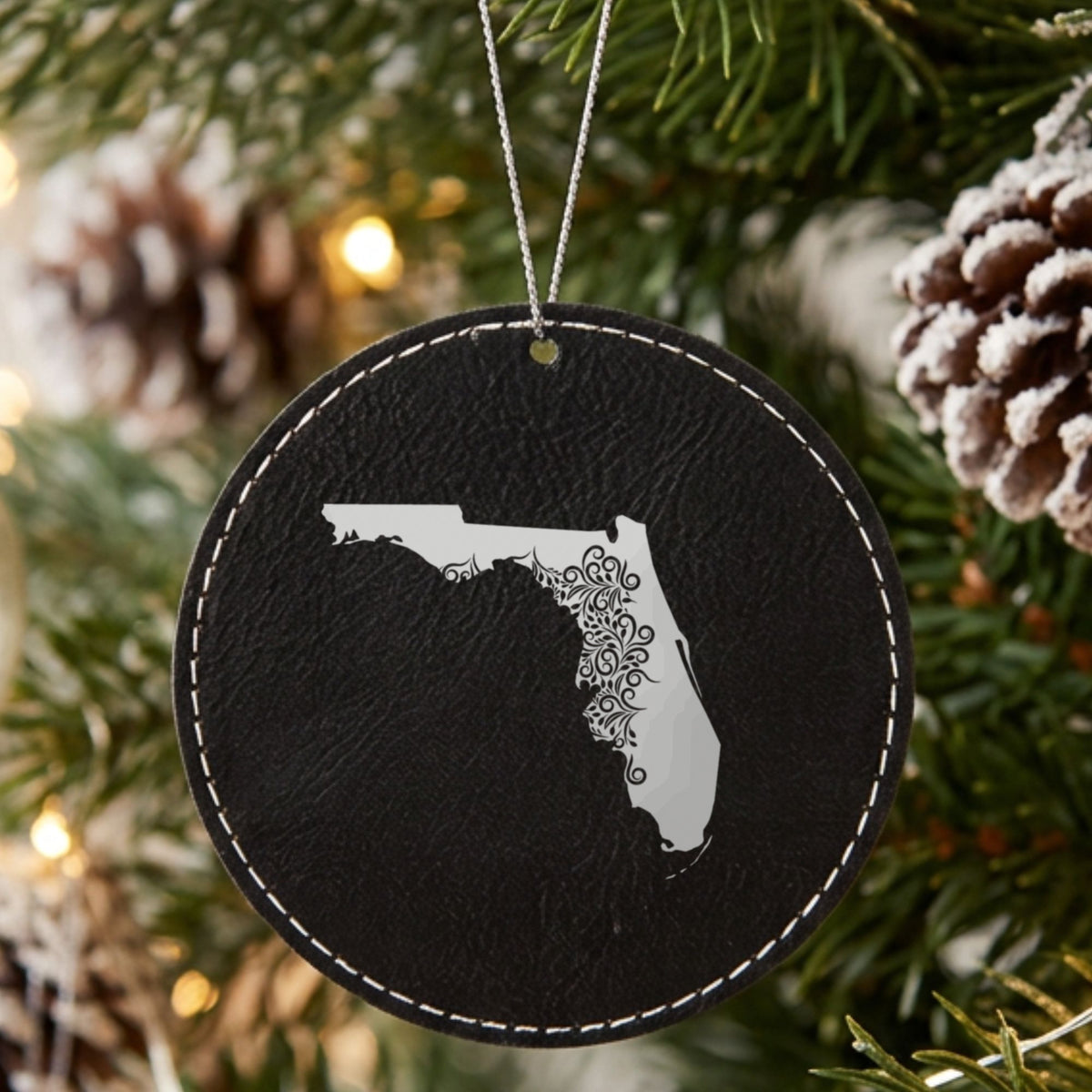 Black leatherette round Christmas ornament laser engraved with the Florida Floral Damask design, hanging on a tree