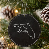 Black leatherette round Christmas ornament laser engraved with the Florida Hand-Drawn Love design, hanging on a tree