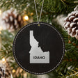 Black leatherette round Christmas ornament laser engraved with the Idaho Bold State Name design, hanging on a tree