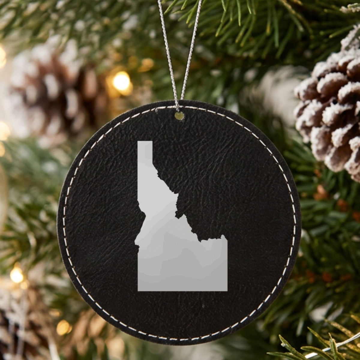 Black leatherette round Christmas ornament laser engraved with the Idaho Engraved State design, hanging on a tree