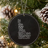 Black leatherette round Christmas ornament laser engraved with the Idaho Word Cloud design, hanging on a tree