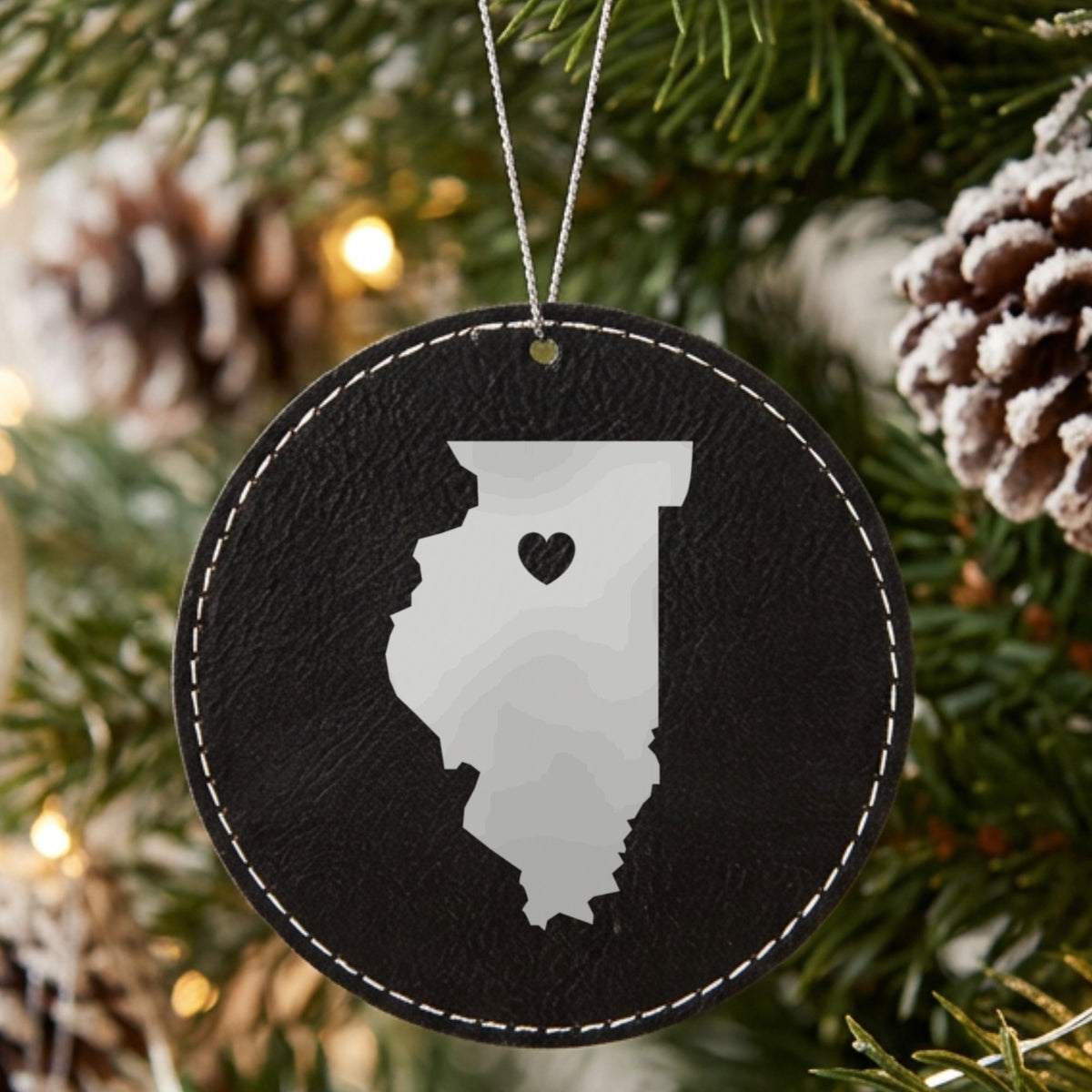 Black leatherette round Christmas ornament laser engraved with the Illinois Heart Accent design, hanging on a tree