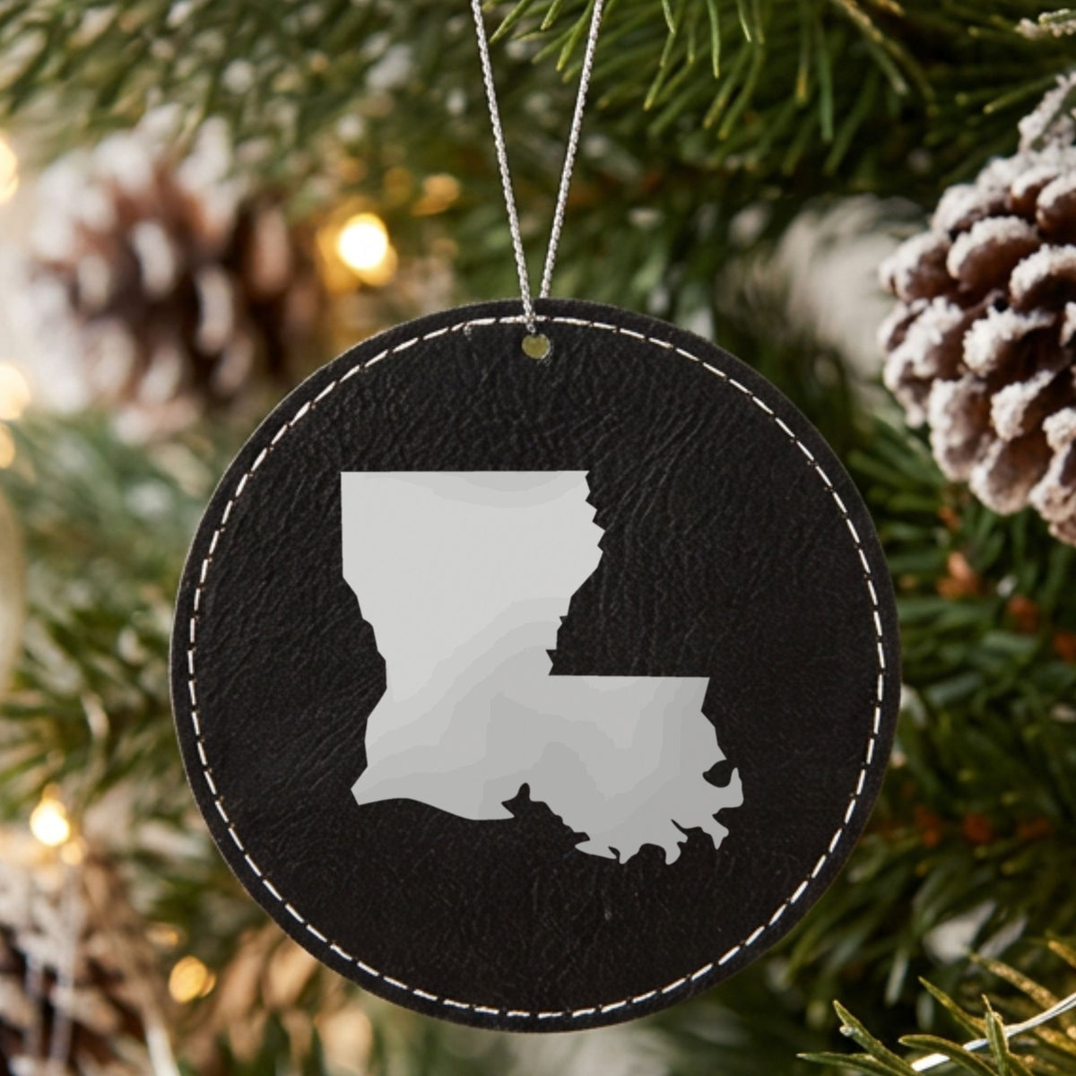Black leatherette round Christmas ornament laser engraved with the Louisiana Engraved State design, hanging on a tree