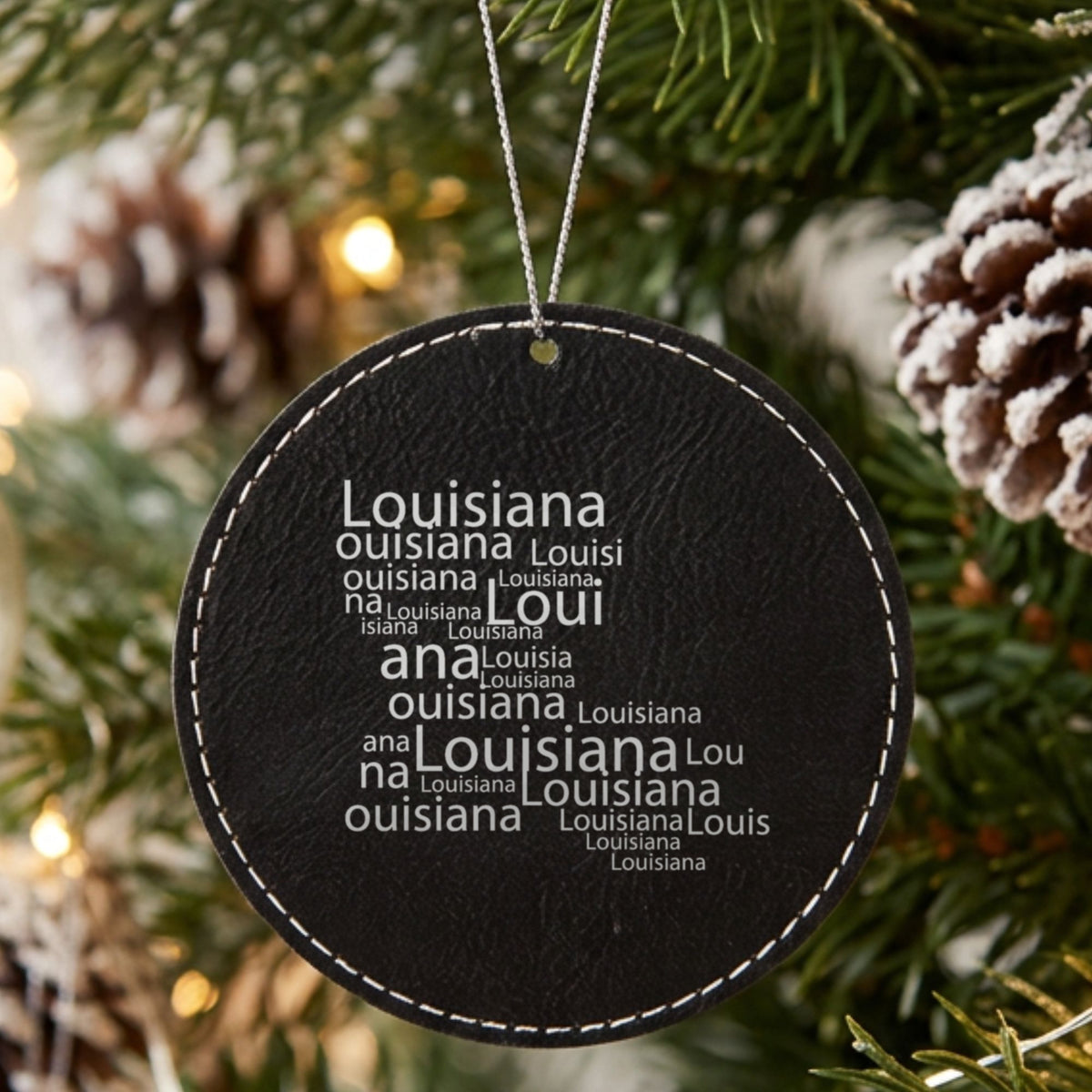 Black leatherette round Christmas ornament laser engraved with the Louisiana Word Cloud design, hanging on a tree
