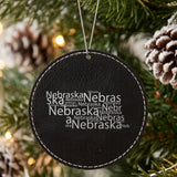 Black leatherette round Christmas ornament laser engraved with the Nebraska Word Cloud design, hanging on a tree