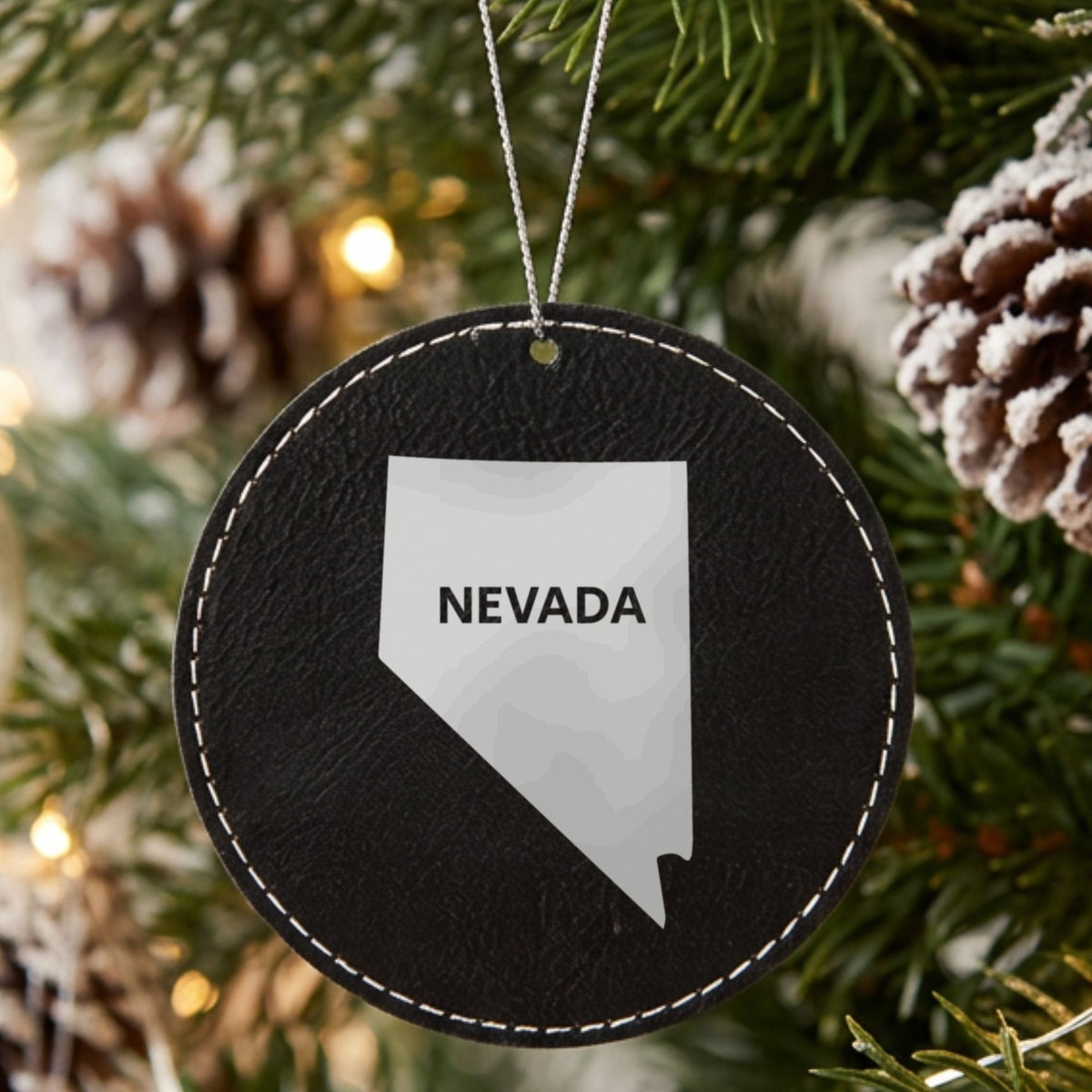 Black leatherette round Christmas ornament laser engraved with the Nevada Bold State Name design, hanging on a tree