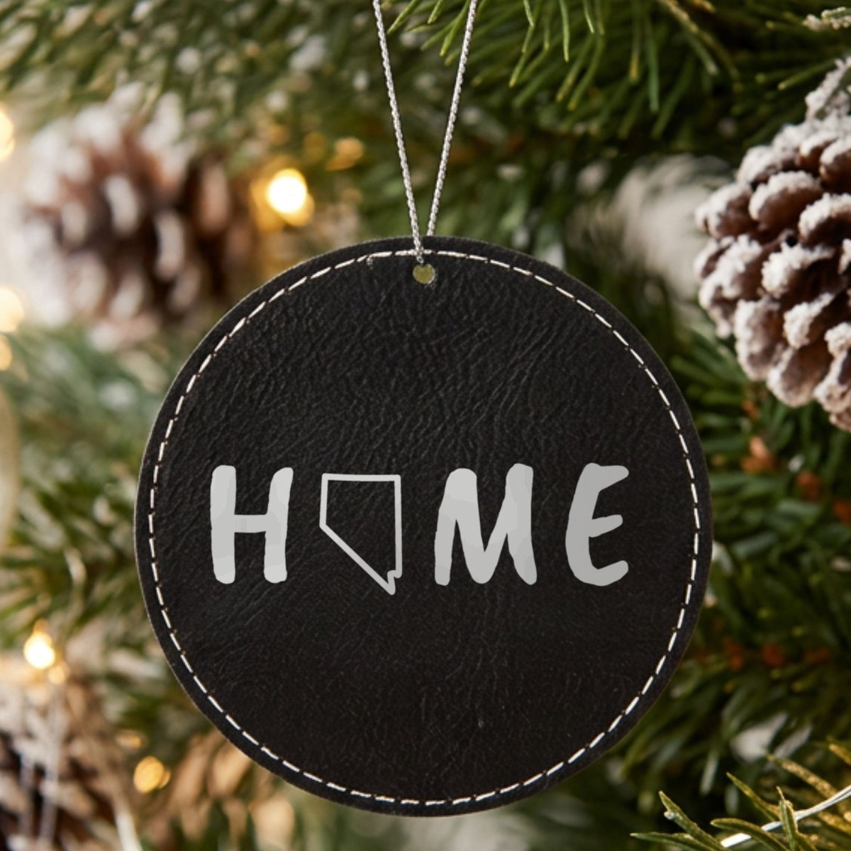 Black leatherette round Christmas ornament laser engraved with the Nevada HOME Outline design, hanging on a tree