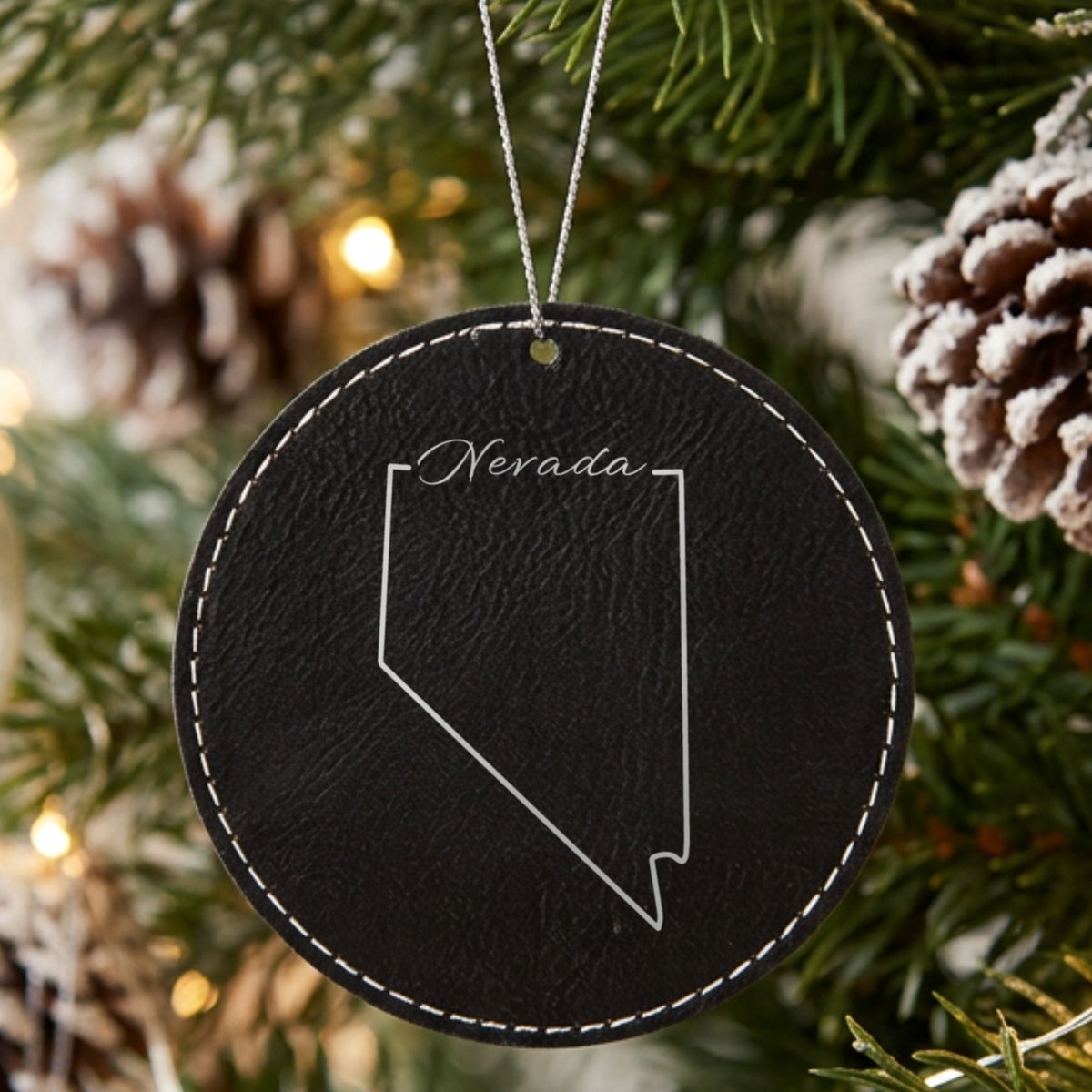Black leatherette round Christmas ornament laser engraved with the Nevada Nevada Script design, hanging on a tree