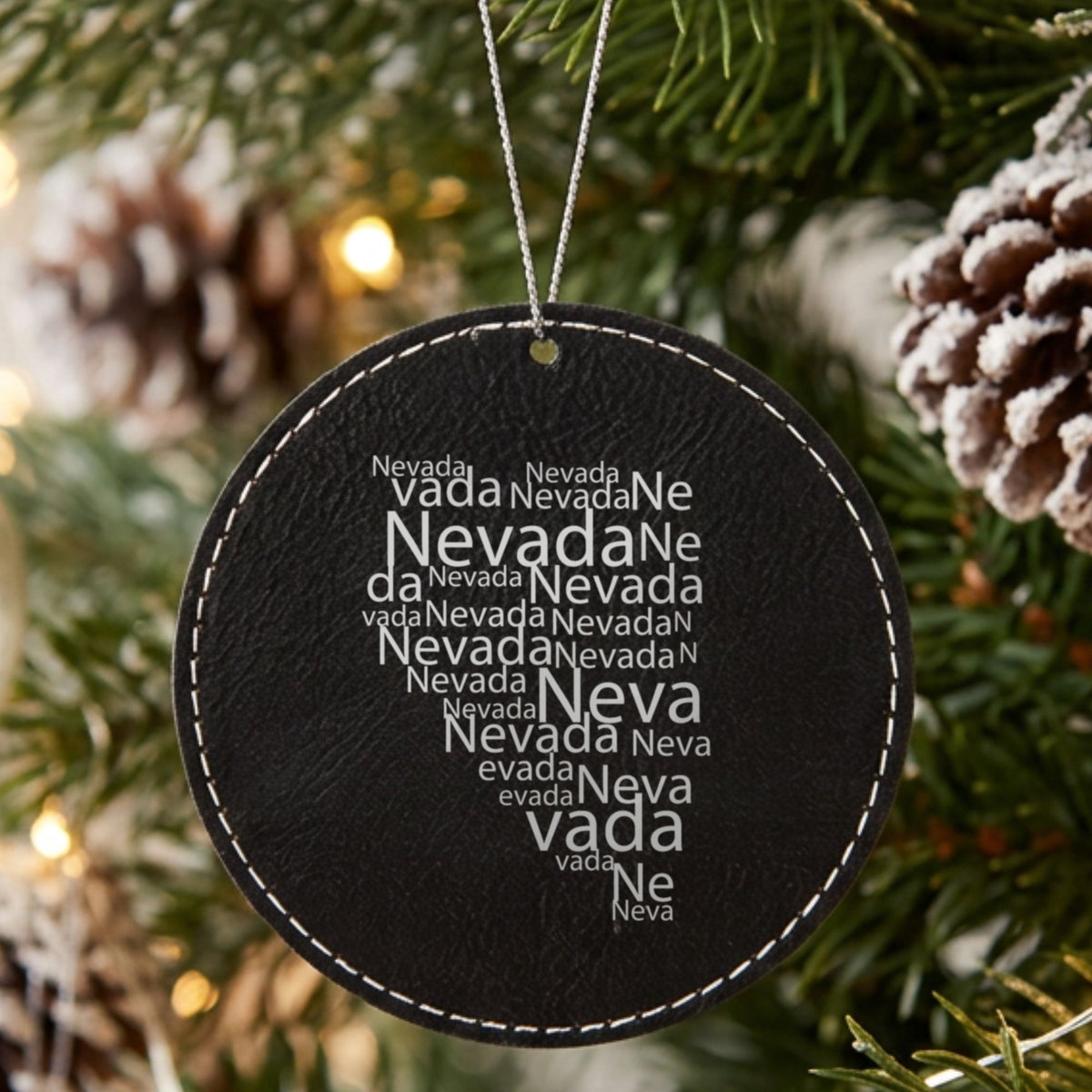 Black leatherette round Christmas ornament laser engraved with the Nevada Word Cloud design, hanging on a tree