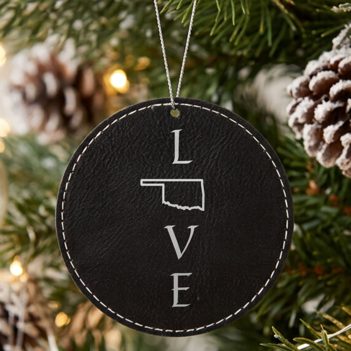 Black leatherette round Christmas ornament laser engraved with the Oklahoma LOVE Stacked design, hanging on a tree