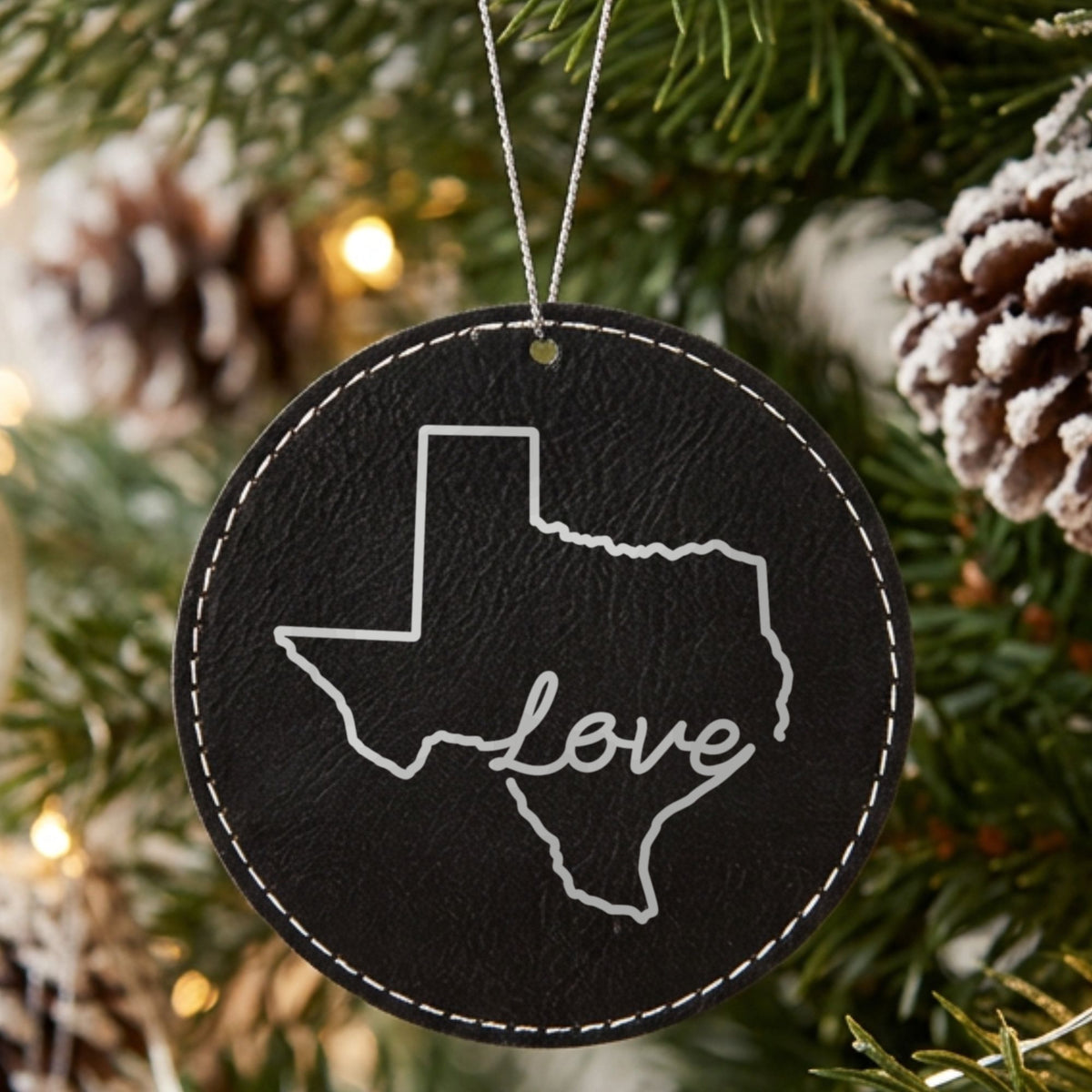 Black leatherette round Christmas ornament laser engraved with the Texas Hand-Drawn Love design, hanging on a tree