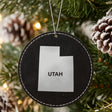 Black leatherette round Christmas ornament laser engraved with the Utah Bold State Name design, hanging on a tree