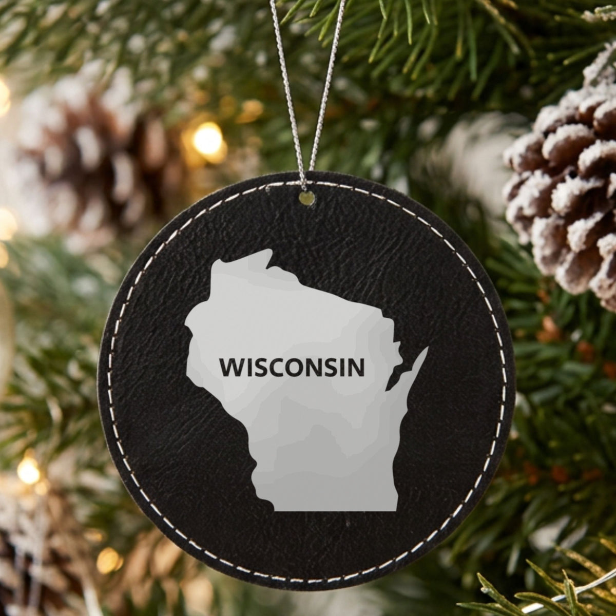 Black leatherette round Christmas ornament laser engraved with the Wisconsin Bold State Name design, hanging on a tree