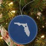 Blue leatherette round Christmas ornament laser engraved with the Florida Heart Accent design, hanging on a tree