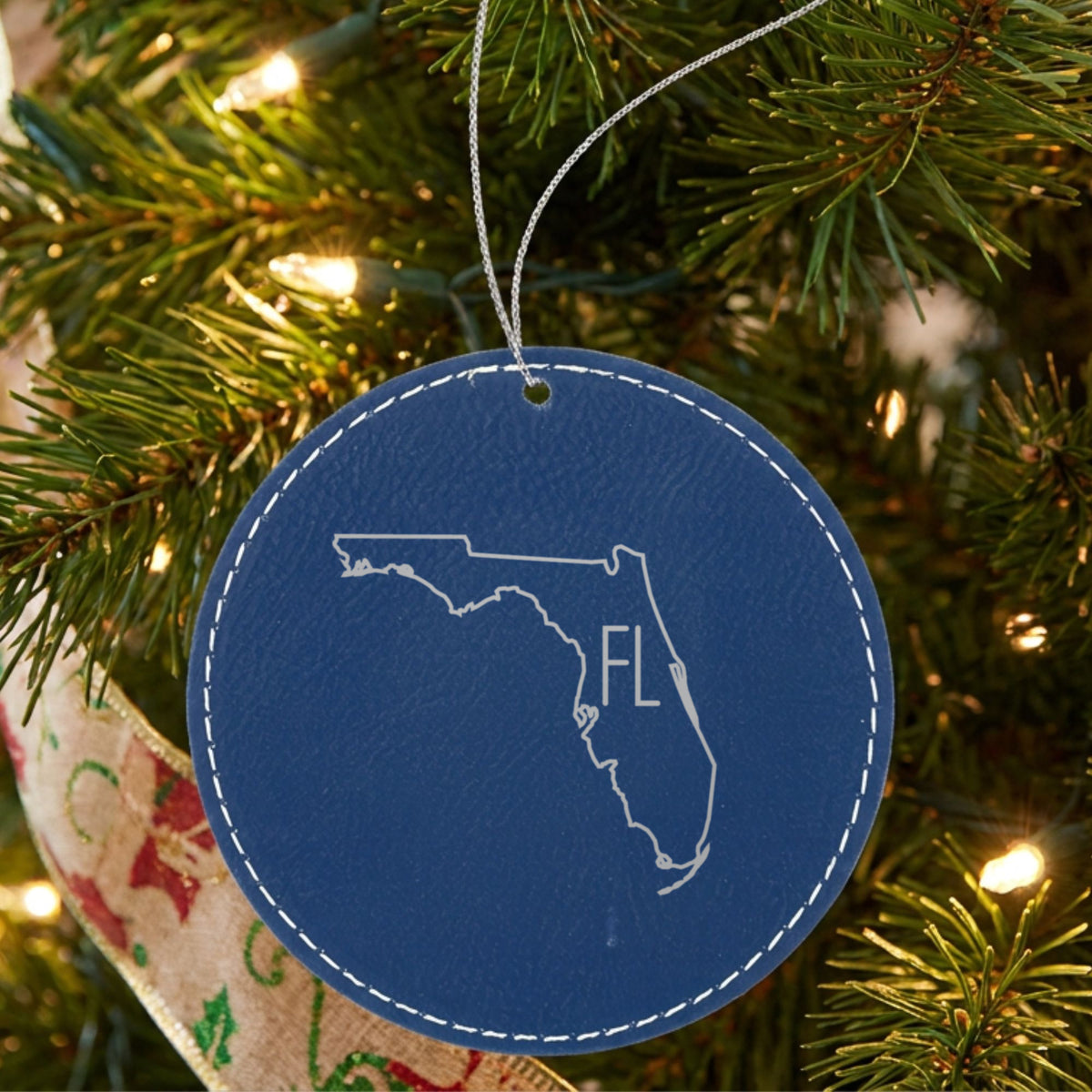 Blue leatherette round Christmas ornament laser engraved with the Florida FL Initials design, hanging on a tree