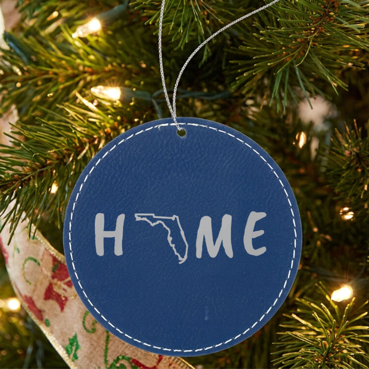 Blue leatherette round Christmas ornament laser engraved with the Florida HOME Outline design, hanging on a tree