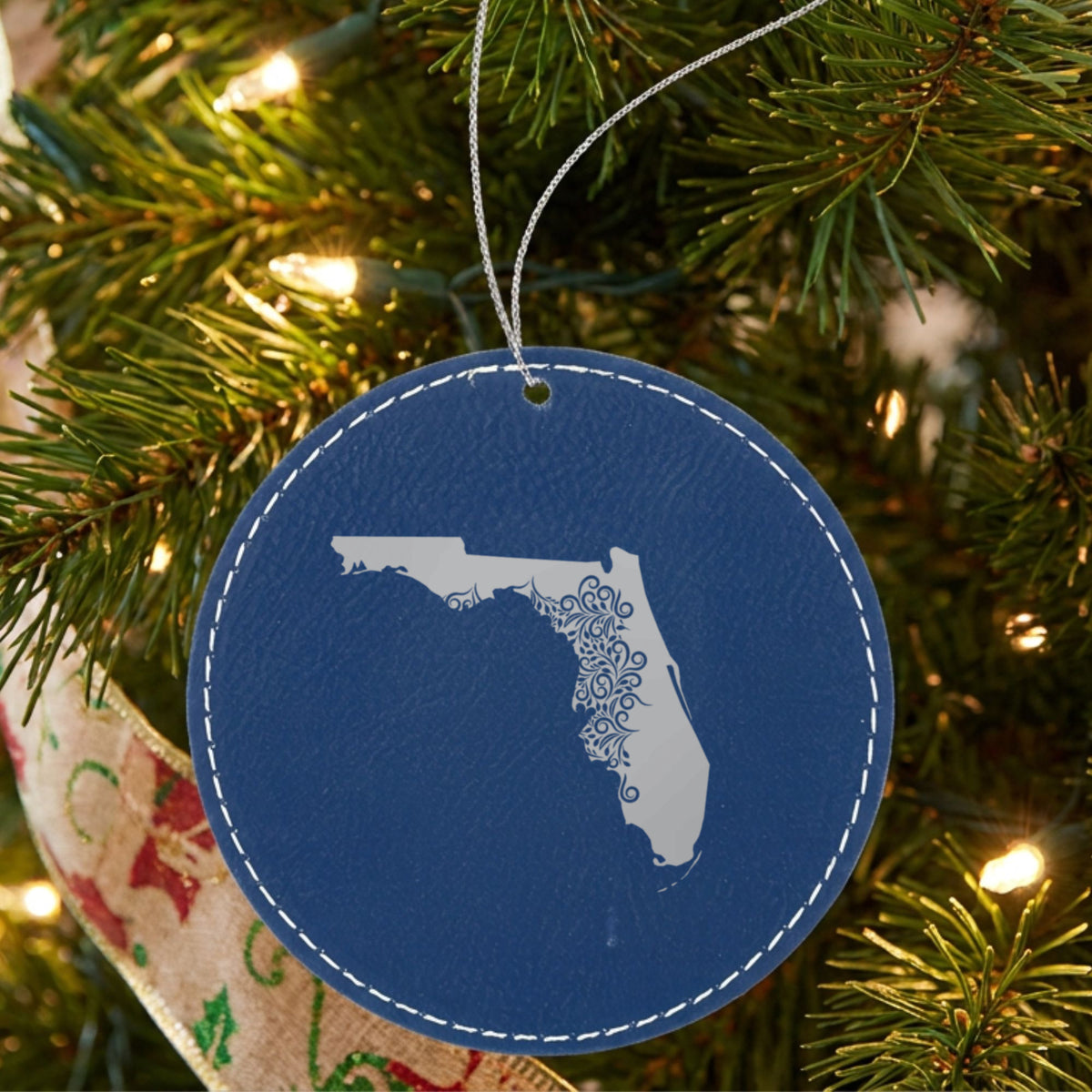 Blue leatherette round Christmas ornament laser engraved with the Florida Floral Damask design, hanging on a tree