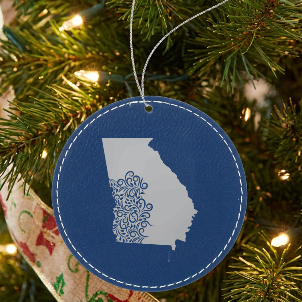 Blue leatherette round Christmas ornament laser engraved with the Georgia Floral Damask design, hanging on a tree