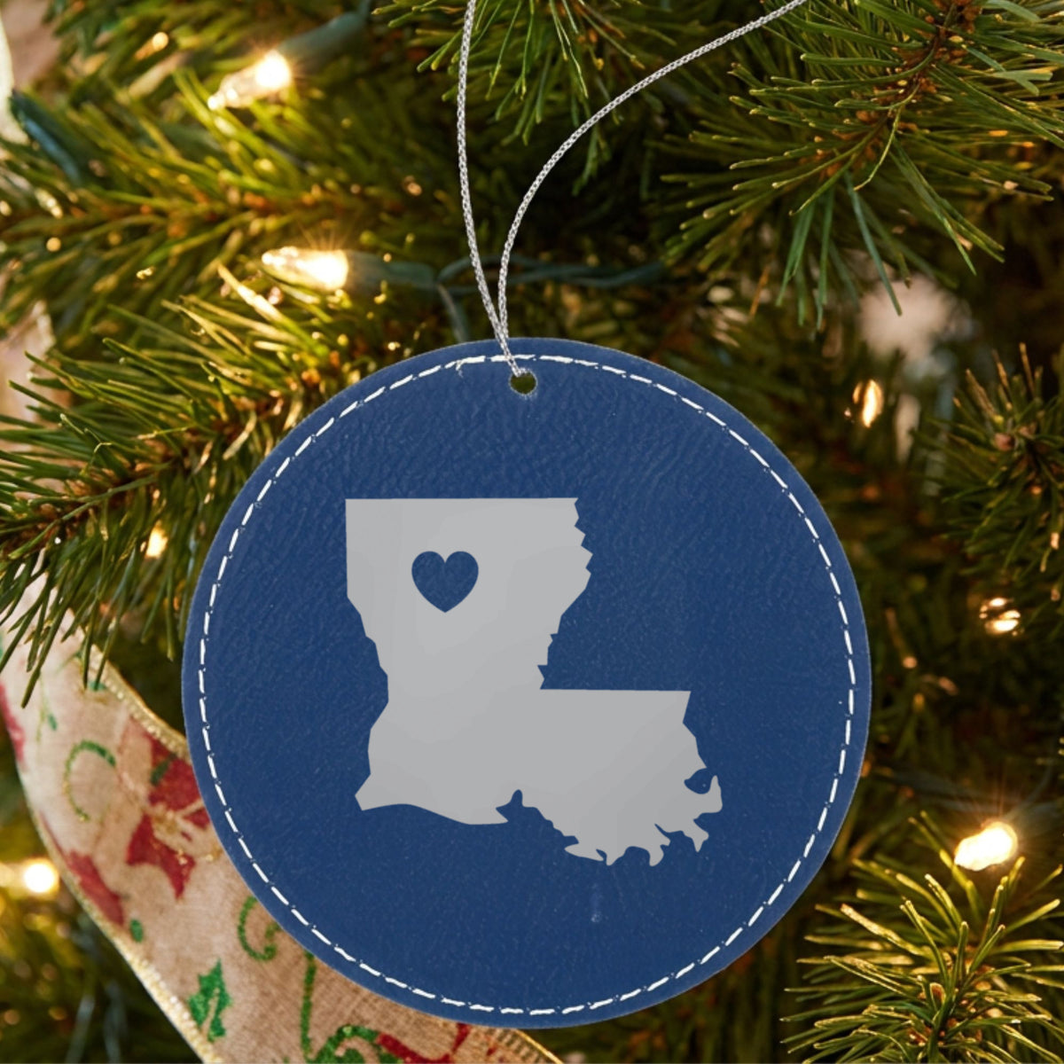 Blue leatherette round Christmas ornament laser engraved with the Louisiana Heart Accent design, hanging on a tree