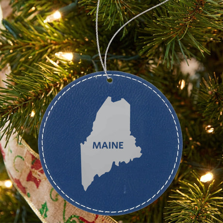 Blue leatherette round Christmas ornament laser engraved with the Maine Bold State Name design, hanging on a tree