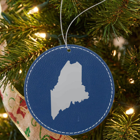 Blue leatherette round Christmas ornament laser engraved with the Maine Engraved State design, hanging on a tree