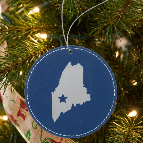 Blue leatherette round Christmas ornament laser engraved with the Maine Star Accent design, hanging on a tree