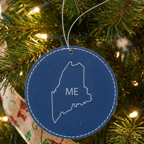 Blue leatherette round Christmas ornament laser engraved with the Maine ME Initials design, hanging on a tree