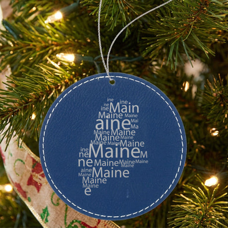 Blue leatherette round Christmas ornament laser engraved with the Maine Word Cloud design, hanging on a tree