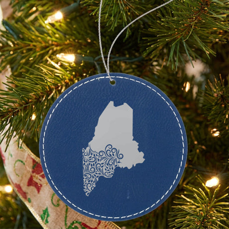Blue leatherette round Christmas ornament laser engraved with the Maine Floral Damask design, hanging on a tree