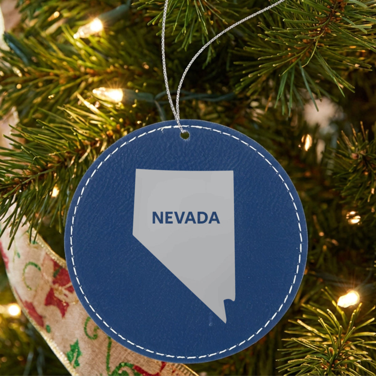 Blue leatherette round Christmas ornament laser engraved with the Nevada Bold State Name design, hanging on a tree