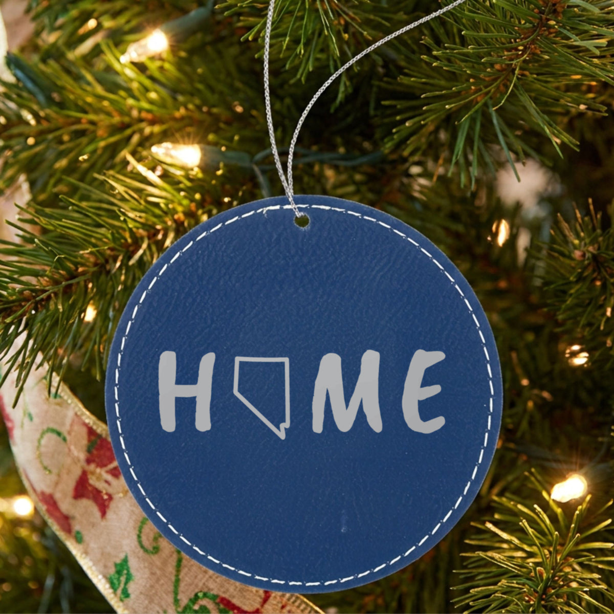 Blue leatherette round Christmas ornament laser engraved with the Nevada HOME Outline design, hanging on a tree
