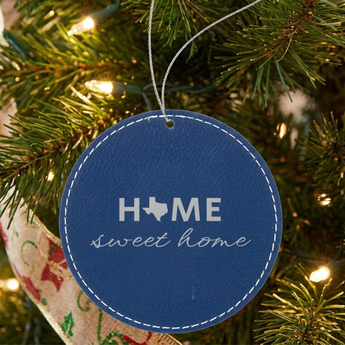 Blue leatherette round Christmas ornament laser engraved with the Texas Home Sweet Home design, hanging on a tree