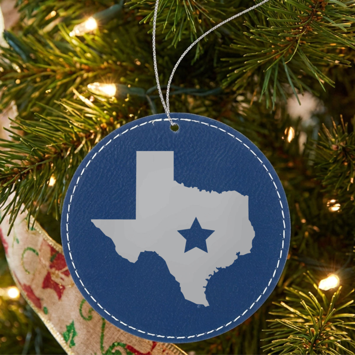 Blue leatherette round Christmas ornament laser engraved with the Texas Star Accent design, hanging on a tree