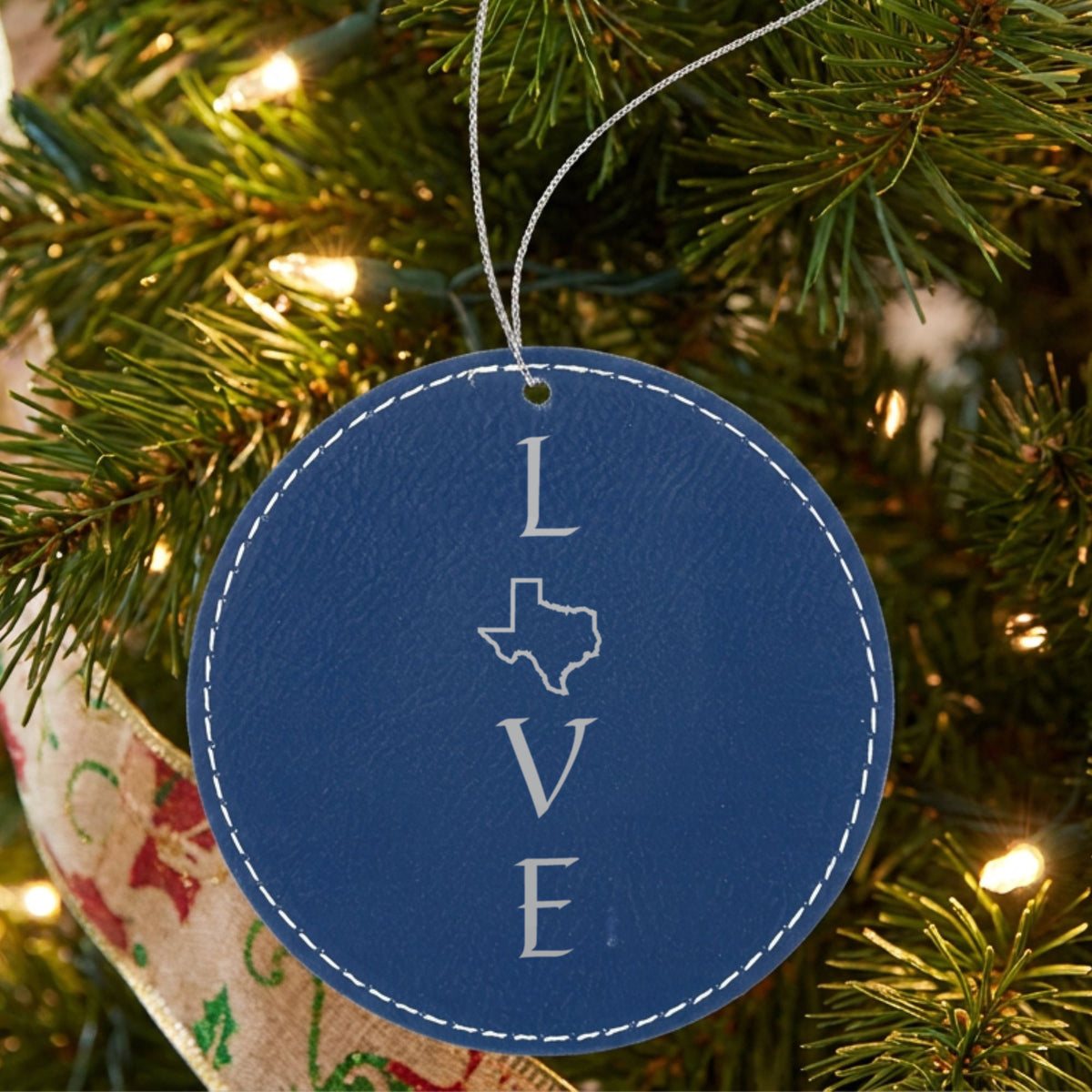 Blue leatherette round Christmas ornament laser engraved with the Texas LOVE Stacked design, hanging on a tree